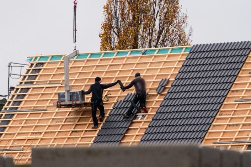 Twee dakwerkers leggen dakpannen op een nieuw dak