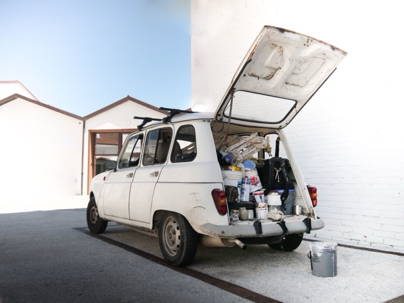 Oude bestelwagen met open koffer vol verfpotten en materiaal