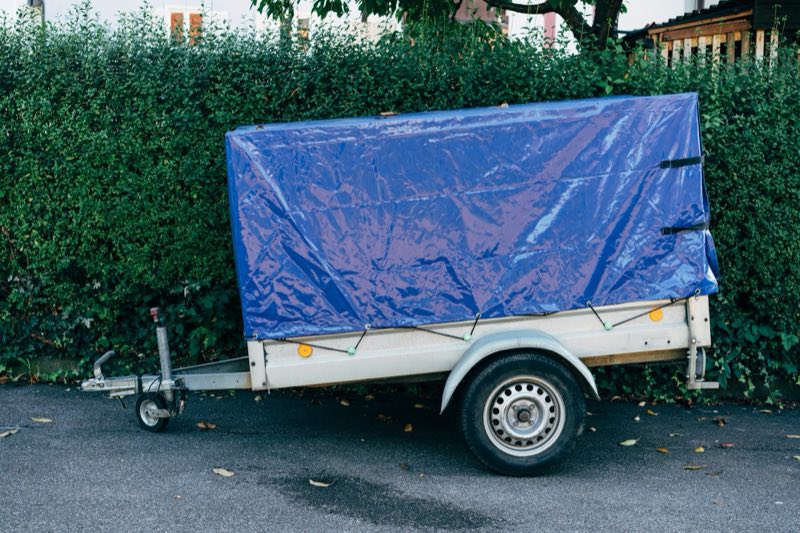 Aanhangwagen met blauw zeil langs een haag