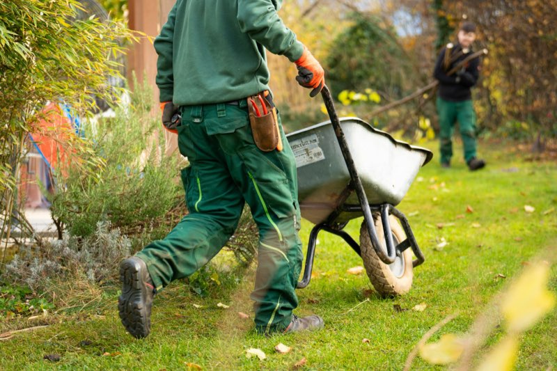 Twee tuinmannen aan het werk in een tuin, een met een kruiwagen